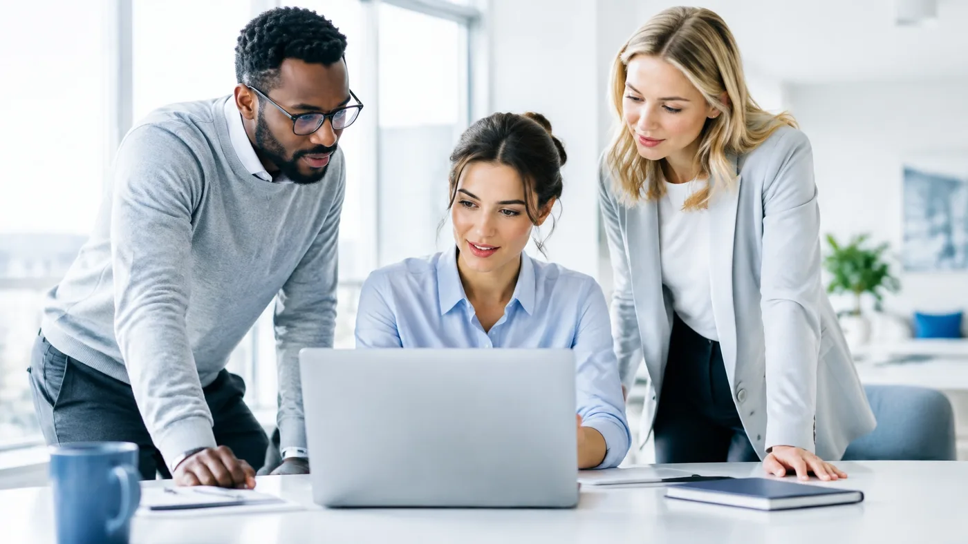 Three professionals reviewing marketing work around a laptop